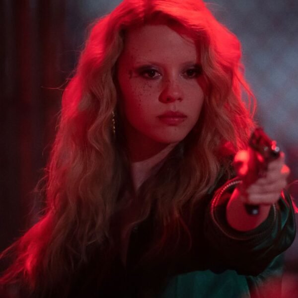 Mia Goth aims a pistol with confidence while bathed in red neon light in MaXXXine.